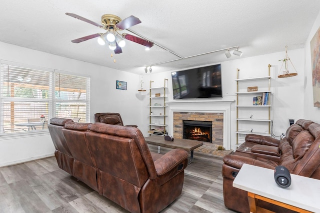 living room with a textured ceiling, track lighting, light wood-type flooring, a fireplace, and ceiling fan