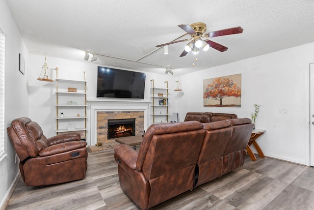 living room with a textured ceiling, light wood-type flooring, ceiling fan, track lighting, and a brick fireplace