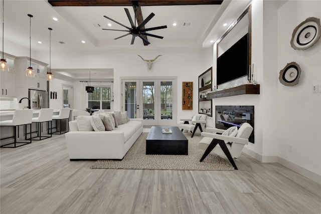 living room with a raised ceiling, ceiling fan, and light hardwood / wood-style flooring