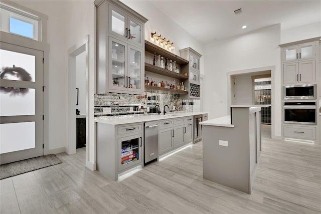 bar featuring beverage cooler, appliances with stainless steel finishes, gray cabinets, and backsplash