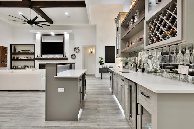 kitchen featuring wine cooler, beamed ceiling, ceiling fan, a kitchen island, and sink