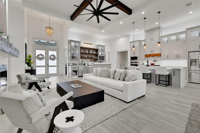 living room with a towering ceiling, french doors, light hardwood / wood-style floors, ceiling fan with notable chandelier, and beam ceiling