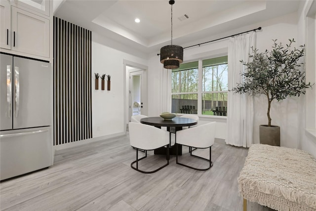 dining space with a raised ceiling and light hardwood / wood-style floors