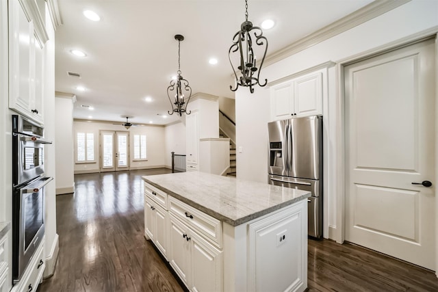 kitchen with appliances with stainless steel finishes, pendant lighting, a kitchen island, white cabinetry, and ceiling fan with notable chandelier