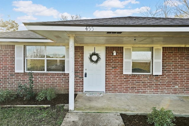 entrance to property with brick siding and roof with shingles