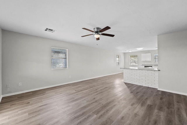 unfurnished living room featuring ceiling fan, wood finished floors, visible vents, and baseboards