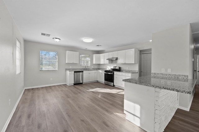 kitchen featuring stone countertops, appliances with stainless steel finishes, a peninsula, under cabinet range hood, and white cabinetry