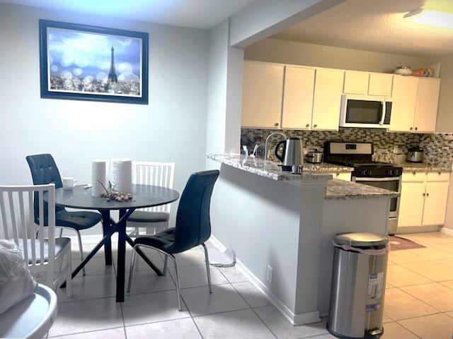 kitchen featuring light stone counters, stainless steel gas stove, light tile patterned flooring, kitchen peninsula, and backsplash