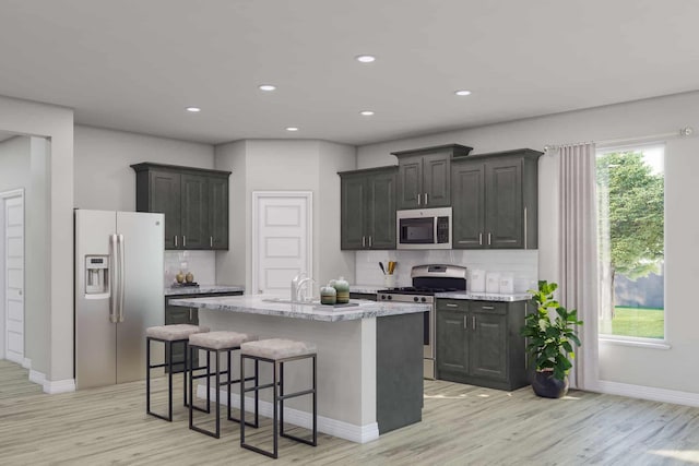 kitchen with a center island with sink, light hardwood / wood-style floors, a kitchen bar, backsplash, and appliances with stainless steel finishes