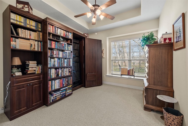 misc room with ceiling fan, a tray ceiling, and light colored carpet