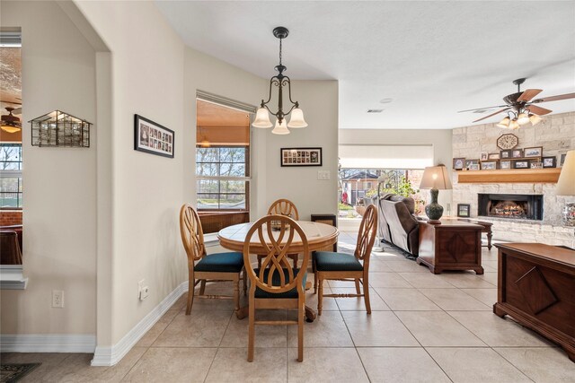 dining space with ceiling fan with notable chandelier, light tile patterned flooring, and a fireplace