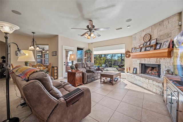 living room with ceiling fan with notable chandelier, a fireplace, a textured ceiling, and light tile patterned floors