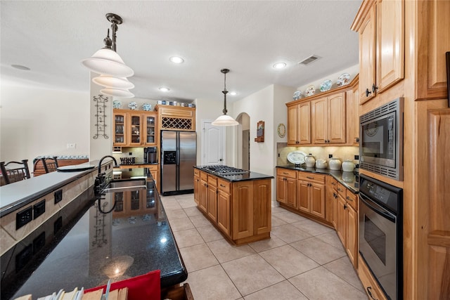 kitchen with appliances with stainless steel finishes, a center island, decorative light fixtures, and light tile patterned floors