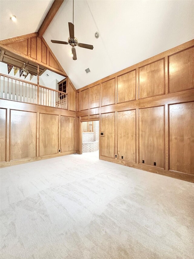 interior space with light colored carpet, ceiling fan, wooden walls, high vaulted ceiling, and beam ceiling