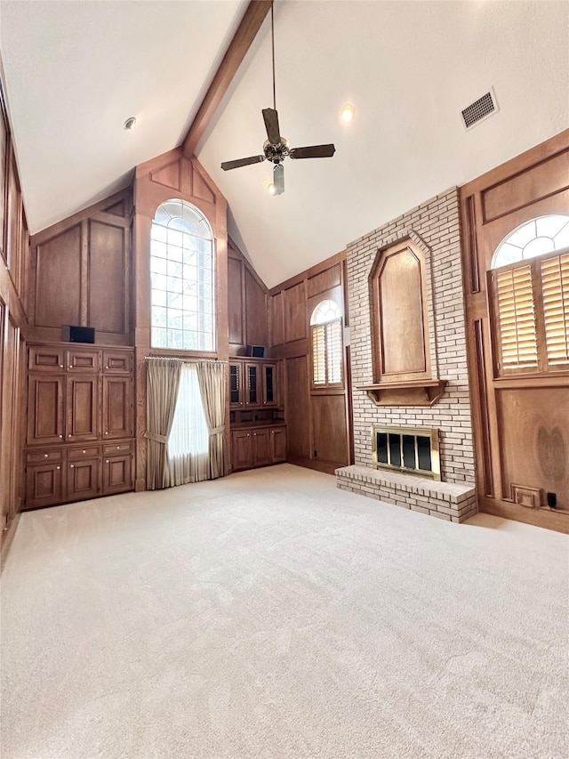 unfurnished living room with wood walls, beamed ceiling, ceiling fan, a brick fireplace, and high vaulted ceiling