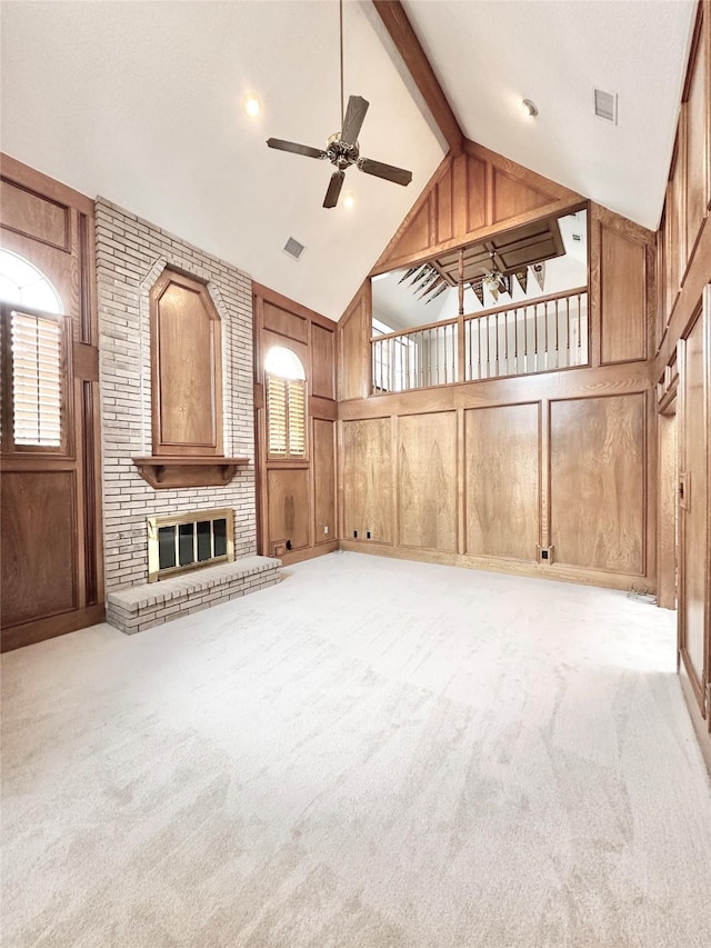 unfurnished living room with wooden walls, beamed ceiling, light carpet, ceiling fan, and a brick fireplace