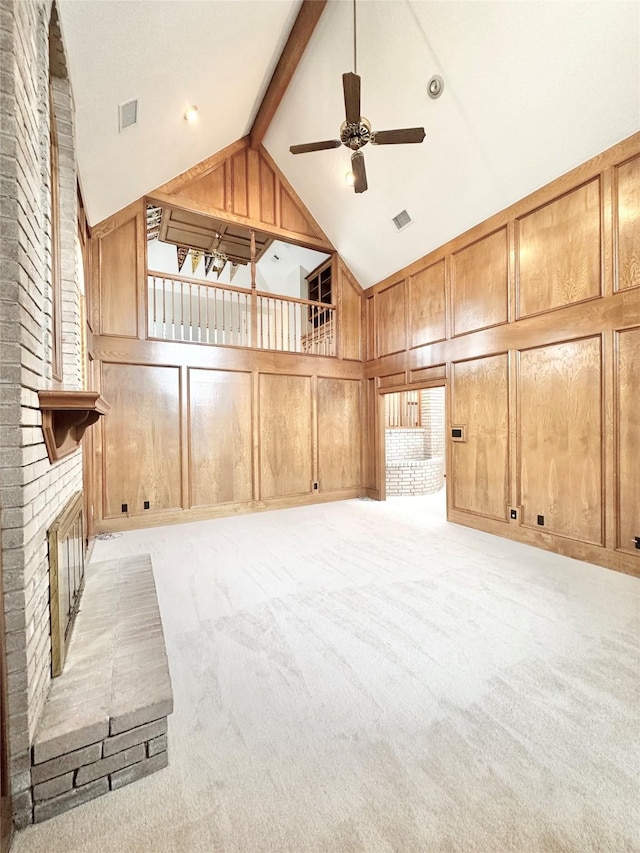 unfurnished living room with a fireplace, light carpet, ceiling fan, wood walls, and beam ceiling