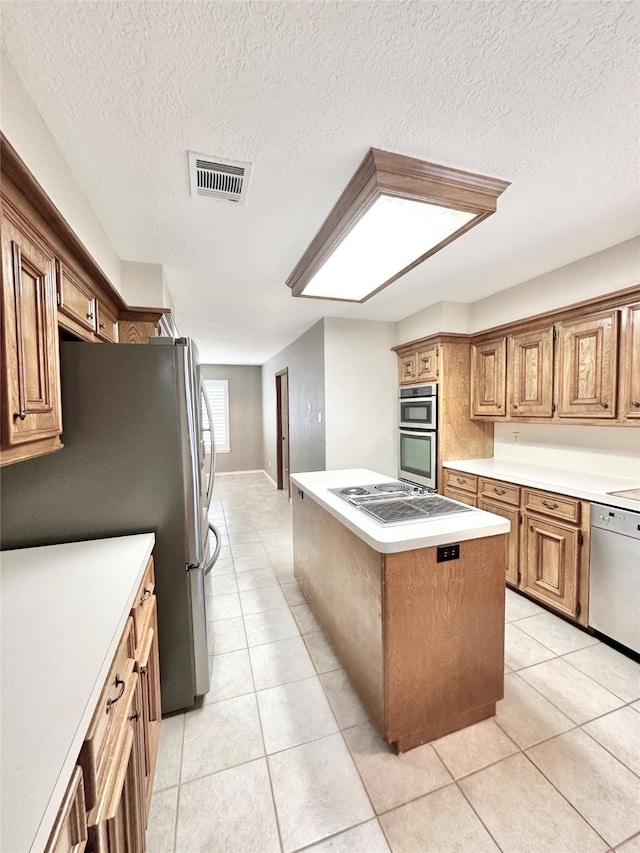 kitchen with stainless steel appliances, a textured ceiling, light tile patterned floors, and a center island