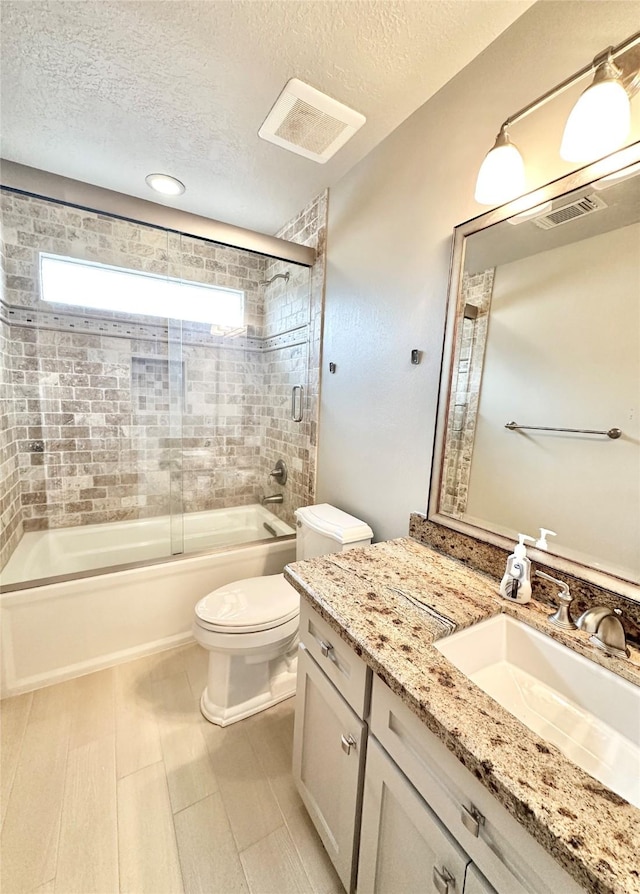 full bathroom featuring a textured ceiling, shower / bath combination with glass door, vanity, and toilet