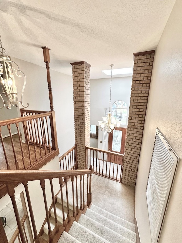 stairway with ornate columns, an inviting chandelier, a textured ceiling, and carpet floors