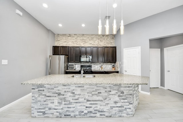 kitchen with sink, hanging light fixtures, light stone countertops, a kitchen island with sink, and stainless steel fridge