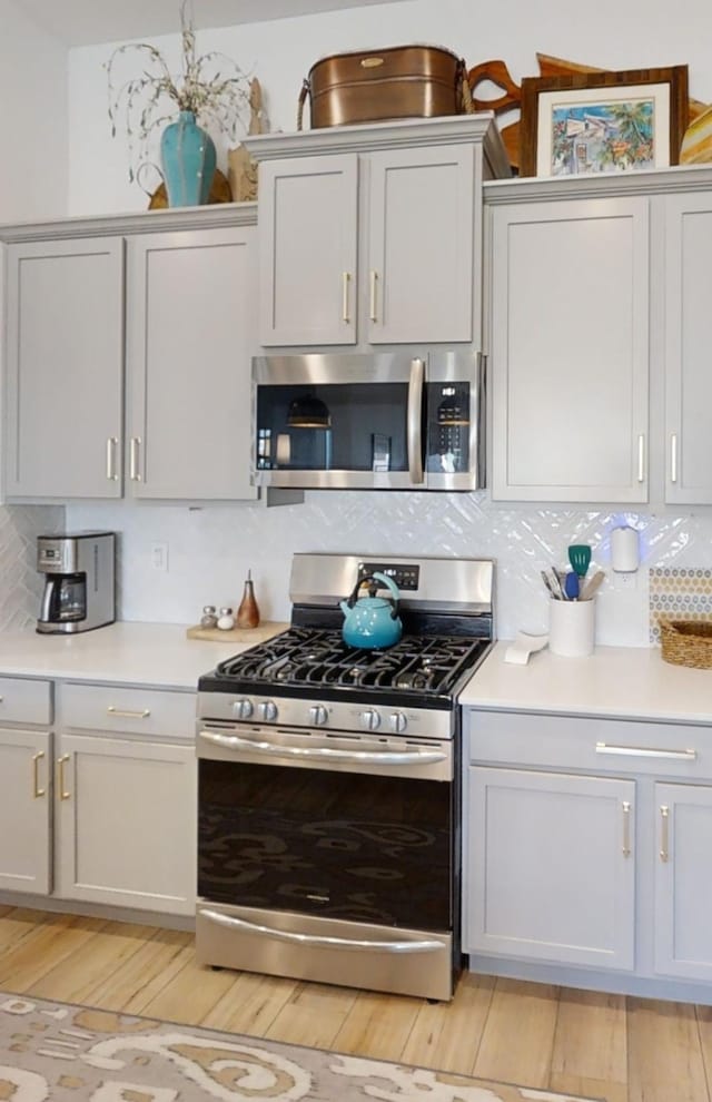 kitchen with light wood-type flooring, tasteful backsplash, and appliances with stainless steel finishes