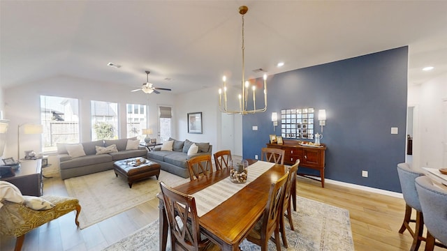 dining area with ceiling fan with notable chandelier, light hardwood / wood-style floors, and vaulted ceiling