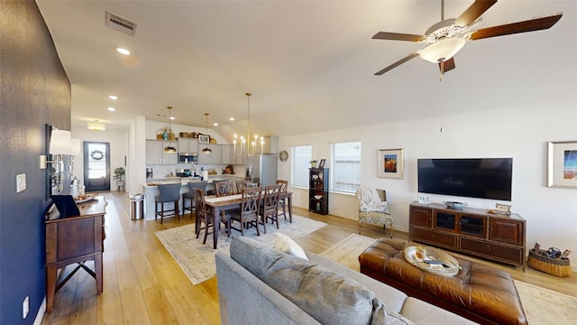 living room with ceiling fan with notable chandelier, light wood-type flooring, and lofted ceiling