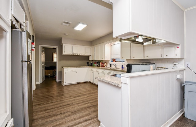 kitchen with dark wood-type flooring, white cabinetry, stainless steel fridge, kitchen peninsula, and backsplash