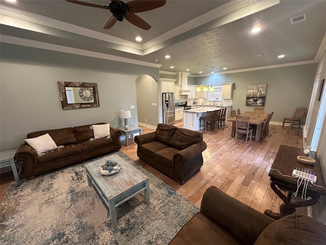 living room featuring sink, crown molding, light hardwood / wood-style flooring, a raised ceiling, and ceiling fan