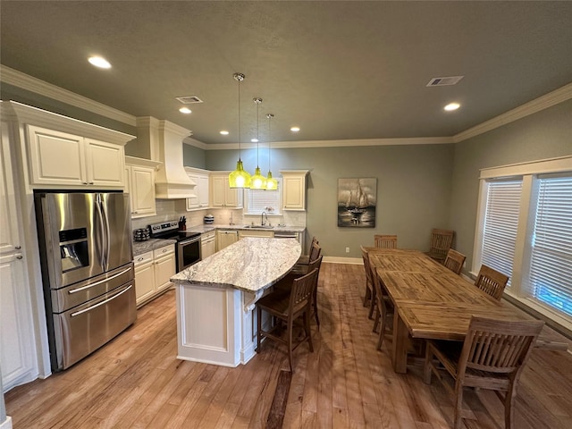 kitchen featuring light stone counters, hanging light fixtures, a kitchen island, custom range hood, and stainless steel appliances