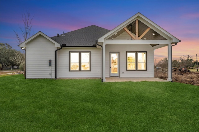 back house at dusk with a patio and a lawn