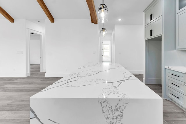 kitchen featuring light stone countertops, light hardwood / wood-style flooring, a center island, decorative light fixtures, and beamed ceiling