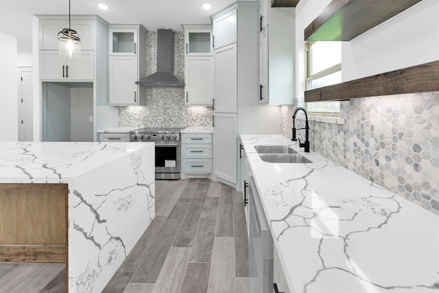 kitchen featuring appliances with stainless steel finishes, pendant lighting, white cabinets, wall chimney range hood, and sink