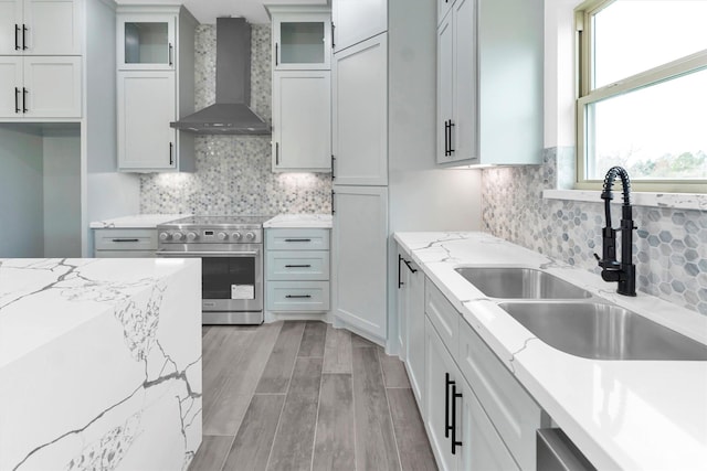 kitchen featuring stainless steel appliances, white cabinets, wall chimney range hood, and sink