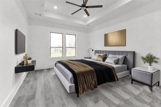 bedroom featuring ceiling fan, light hardwood / wood-style floors, and a tray ceiling