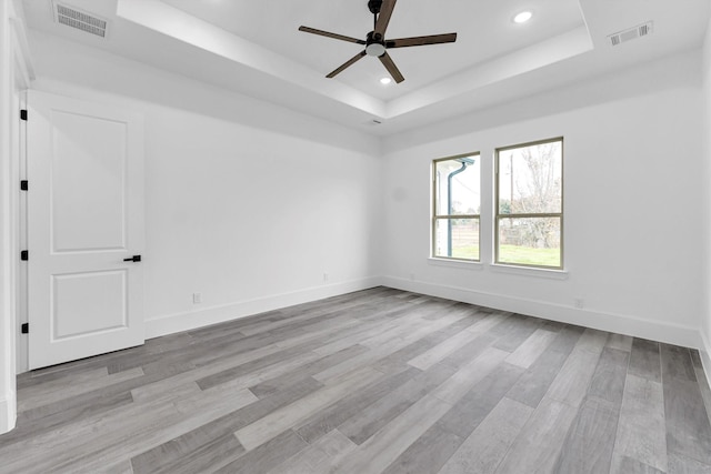 unfurnished room featuring a raised ceiling, ceiling fan, and light wood-type flooring