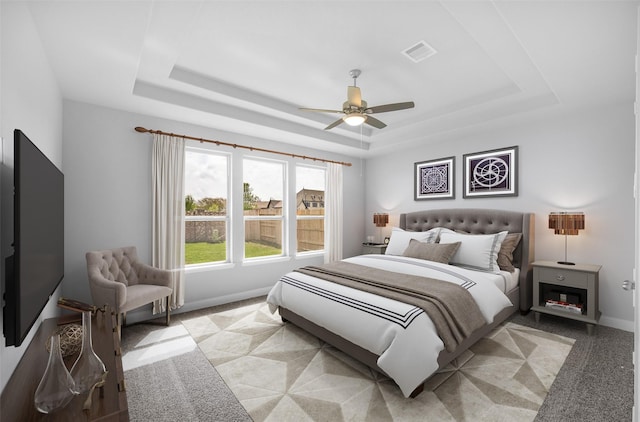 carpeted bedroom with ceiling fan and a raised ceiling