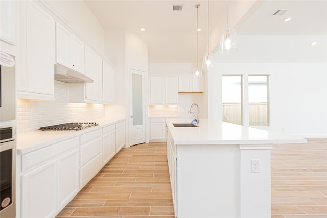 kitchen featuring sink, stainless steel appliances, white cabinets, hanging light fixtures, and a center island with sink