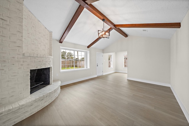 unfurnished living room with hardwood / wood-style flooring, a fireplace, vaulted ceiling with beams, and a notable chandelier