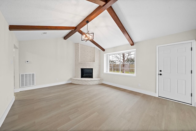 unfurnished living room featuring a fireplace, lofted ceiling with beams, light hardwood / wood-style floors, and a notable chandelier