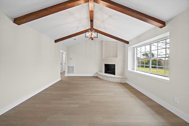 unfurnished living room with an inviting chandelier, a fireplace, lofted ceiling with beams, and light hardwood / wood-style floors