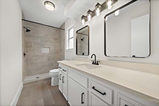 bathroom featuring hardwood / wood-style flooring, a tile shower, vanity, and toilet