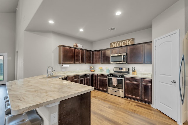 kitchen with stainless steel appliances, kitchen peninsula, dark brown cabinetry, sink, and light hardwood / wood-style flooring