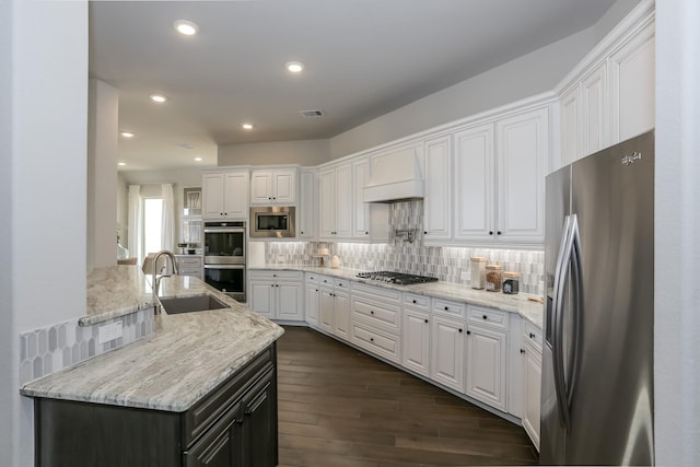 kitchen featuring custom exhaust hood, stainless steel appliances, light stone counters, sink, and white cabinetry