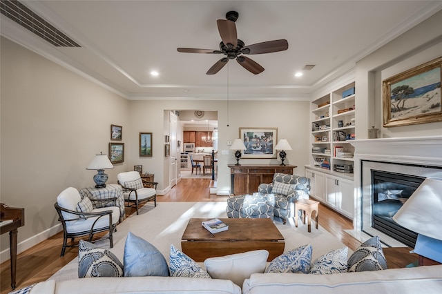 living room with ceiling fan, crown molding, built in features, and light hardwood / wood-style flooring