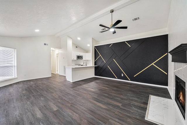 unfurnished living room with dark wood-type flooring, a textured ceiling, lofted ceiling with beams, a high end fireplace, and ceiling fan