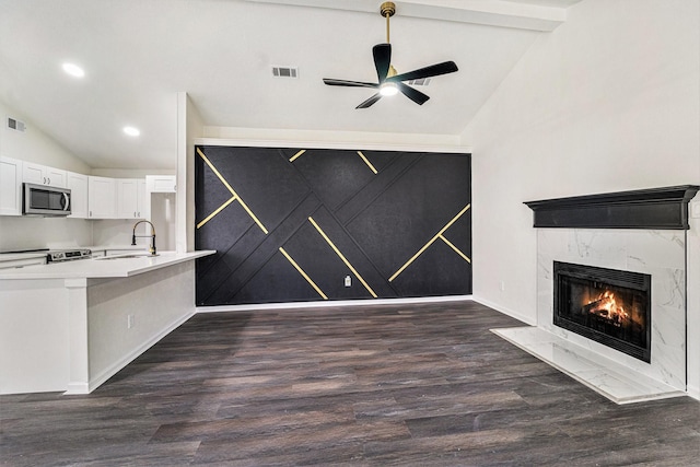 unfurnished living room with sink, a fireplace, ceiling fan, dark hardwood / wood-style floors, and lofted ceiling with beams