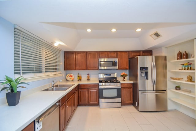 kitchen with appliances with stainless steel finishes, vaulted ceiling, sink, and a tray ceiling