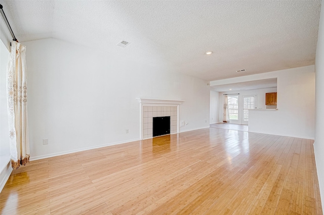 unfurnished living room featuring light hardwood / wood-style floors, a textured ceiling, a tiled fireplace, and vaulted ceiling